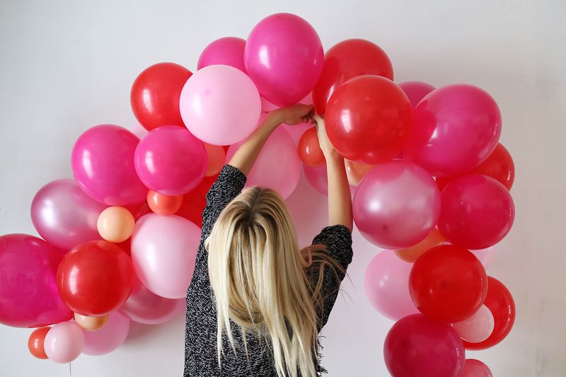 a blonde woman hanging up the balloon arch on the wall